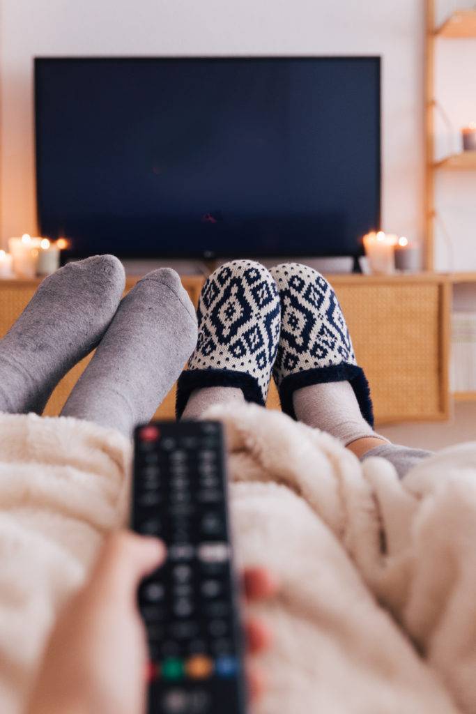 Dos personas viendo la televisión tapados con una manta en un salón decorado con velas